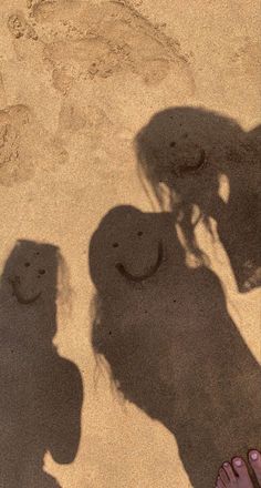 two people standing next to each other with their shadows on the ground and one person's feet in the sand