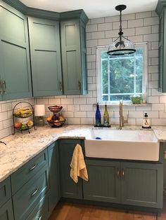 a kitchen with green cabinets and marble counter tops, white tile backsplash and wooden flooring