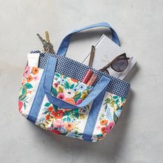 a blue and white flowered bag with scissors, sunglasses and other items in it