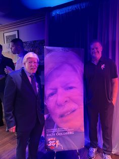 two men standing in front of a large poster on the floor next to each other