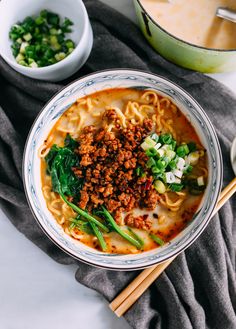 a bowl filled with noodles, meat and vegetables next to chopsticks on a table