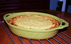 a green casserole dish sitting on top of a wooden table covered in cheese