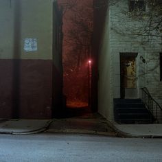 an open door with a red light shining in the dark at night on a city street