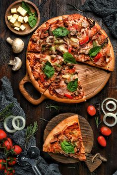 a pizza with one slice missing from it on a cutting board next to other food items