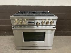 a stainless steel stove with four burners and two oven doors on each side, in front of a brick wall