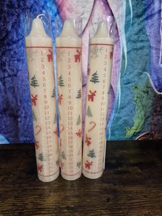 three candles sitting on top of a wooden table next to a wallpapered background