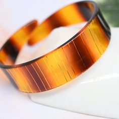 "Vintage brown, orange and gold cuff bracelet with a faux tortoiseshell look. Has thin bands of gold that catch the light. Really great vintage piece! Measures .75 inch at its thickest. Standard 2.5 inch diameter. In good vintage condition. There is mild surface scratching to the plastic commensurate with age normal wear. Check out our other vintage and antique jewelry pieces www.etsy.com/shop/MyMenagerieVintage Free (domestic) shipping. To shop for new handmade jewelry using vintage findings or 1980s Costume, 80s Jewelry, Vintage Cuff Bracelet, Plastic Bangles, Bangles Style, Gold Bracelet Cuff, Gold Cuffs, Unique Bracelets, Gold Fashion