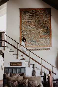 a woman is standing in front of a large tapestry on the wall above a couch