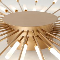 a round light fixture with many lights on it's sides and gold colored metal rods