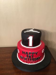 a black and red birthday cake with the number one on it's top is sitting on a wooden table