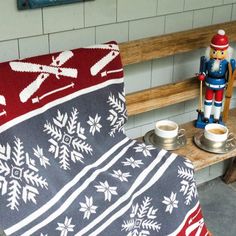 a blanket sitting on top of a wooden bench next to a cup and nutcracker