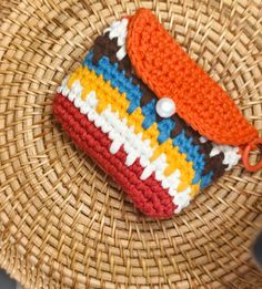 a small crocheted pouch sitting on top of a wicker basket with an orange handle