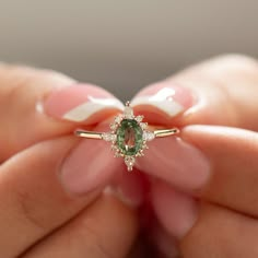 a woman's hand holding an engagement ring with a green gemstone in it