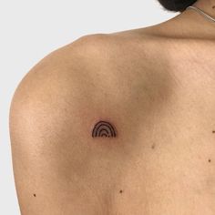 the back of a person's shoulder with a small, black circle tattoo on it