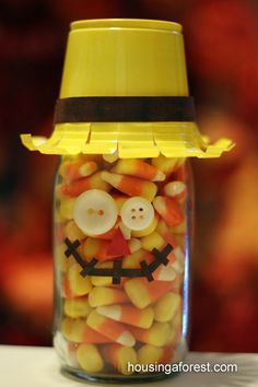 a glass jar filled with candy corn and a smiley face on the lid that has buttons in it