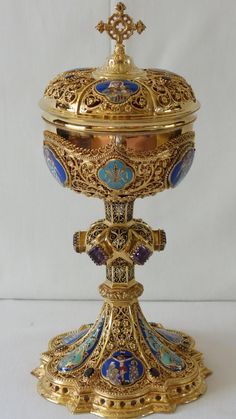 an ornate gold and blue urn with a cross on the top, in front of a white background