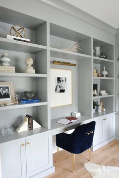 an office with white bookcases and blue velvet chair