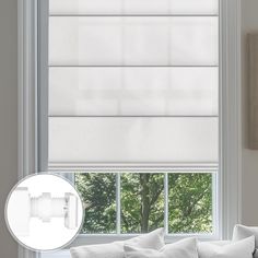 a living room window with white blinds and pillows on the couch in front of it