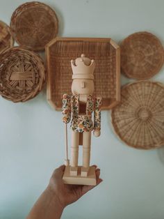 a person holding up a wooden toy in front of some wicker wall hangings