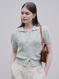 a woman wearing a green sweater and beige pants with a brown bag on her shoulder