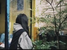 a woman standing in front of a tree next to a yellow building and potted plants