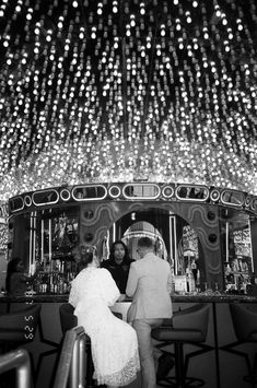 black and white photo of people at bar with chandelier in the ceiling above