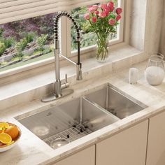 a kitchen sink sitting under a window next to a bowl of oranges and flowers