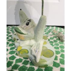 a ceramic figurine sitting on top of a green and white tablecloth covered floor