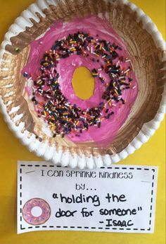 a pink frosted donut sitting on top of a paper plate next to a sign