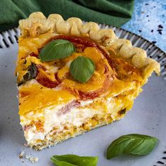 a slice of quiche on a plate with basil leaves