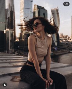 a woman with her hair flying in the wind sitting on a ledge next to a cityscape