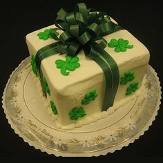 a white cake with green ribbon and shamrocks on it, sitting on a plate