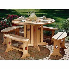 a wooden table with two benches and a vase on the top, in front of some flowers