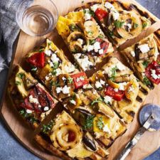 a pizza cut into eight pieces on top of a wooden cutting board next to a glass of water