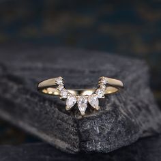 a gold ring with three pear shaped diamonds on it sitting on top of a rock