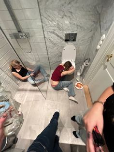 three people sitting on the floor in front of a bathroom mirror with their backs to each other