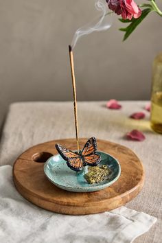 a butterfly incense burner sitting on top of a blue plate next to pink flowers