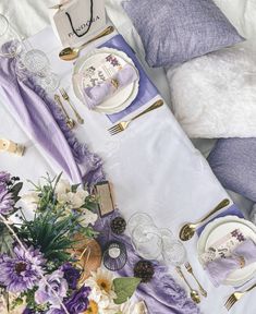 the table is set with purple flowers and white plates, napkins and silverware