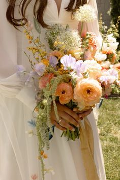 a woman holding a bouquet of flowers in her hands and wearing a white dress with an orange sash