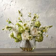 a vase filled with white and green flowers on top of a wooden table next to a wall