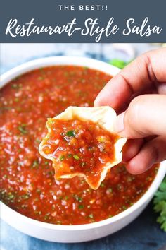 a hand holding a tortilla over a bowl of salsa