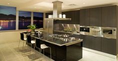 a modern kitchen with stainless steel appliances and large windows overlooking the water at night time