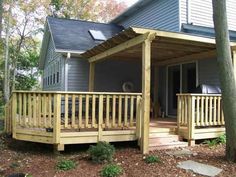 a house with a wooden porch and covered patio area next to trees in front of it