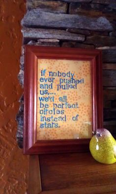 a framed quote is sitting on top of a shelf next to a pear and a stone wall