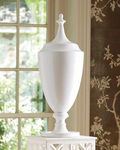 a white urn sitting on top of a table next to a wallpapered window