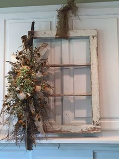 an old window frame is decorated with dried flowers and greenery in front of it