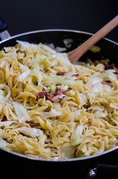 a skillet filled with noodles and vegetables on top of a stove burner next to a wooden spoon