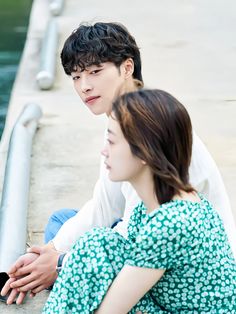 a young man and woman sitting next to each other on the side of a body of water