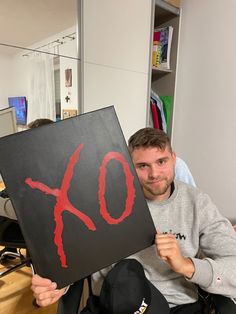 a man sitting in a chair holding up a sign with the word xo painted on it