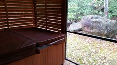 a hot tub sitting in front of a window next to a stone rock and trees